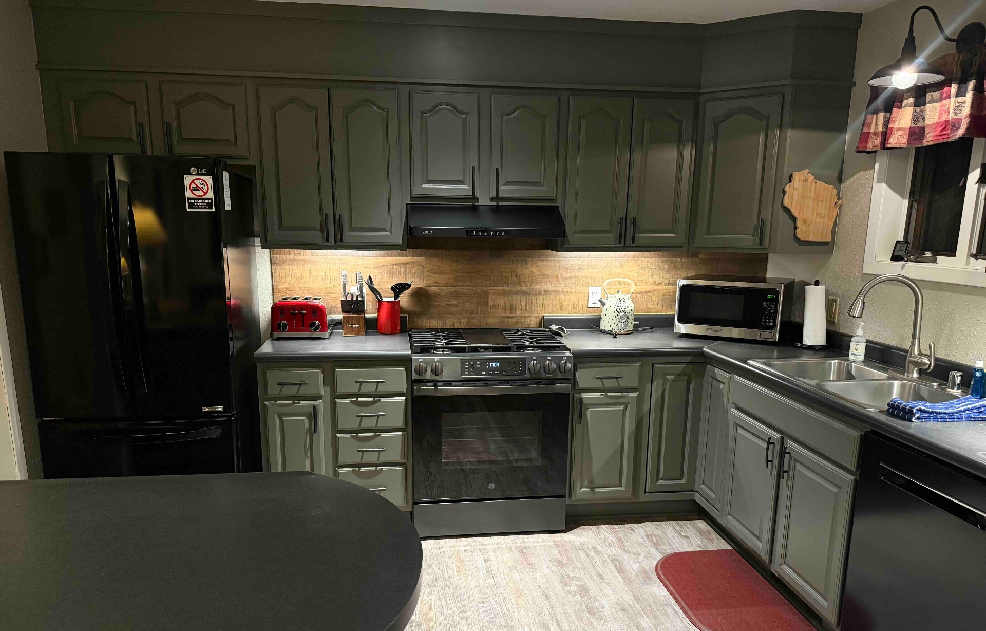 Kitchen with sage-green cabinets, gas range, and wood backsplash